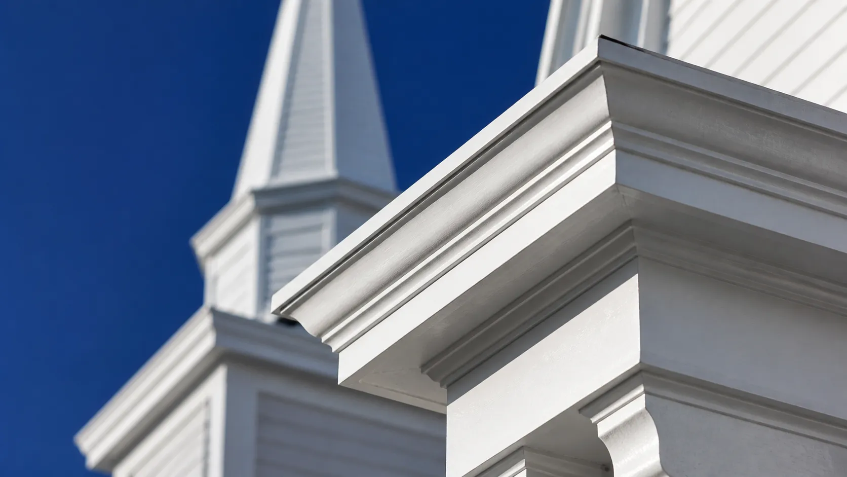 A freshly painted white church steeple and cornice against a clear blue sky